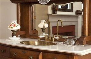 A vintage-style bathroom with a wooden vanity, a brass sink, and a mirror above the sink.