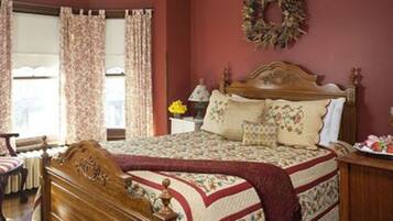 A bedroom with a wooden bed, floral bedding, a chair, a nightstand, and a wall wreath.