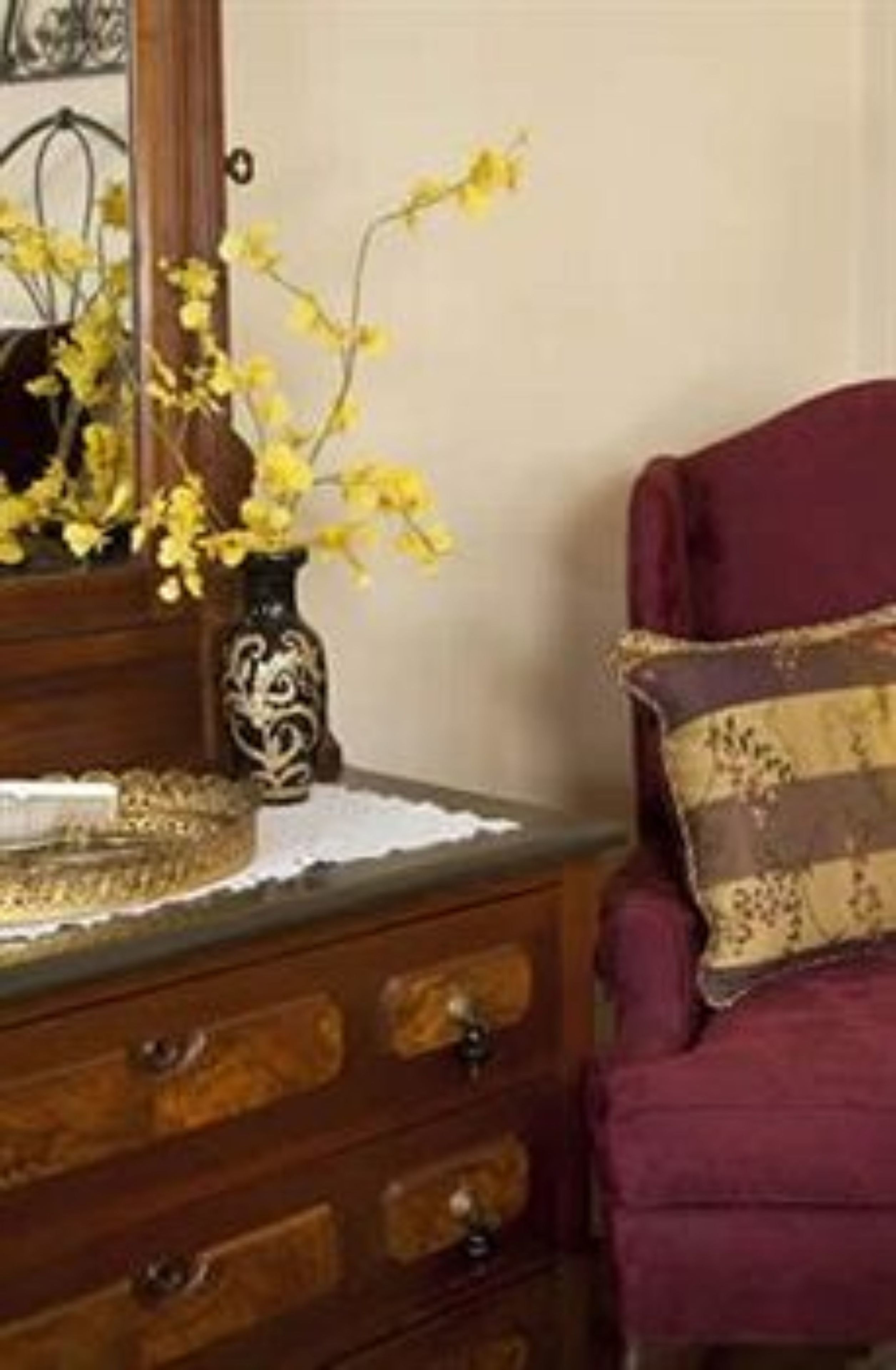 Un comò di legno con un vaso di fiori gialli, una sedia rossa con un cuscino decorato e un elegante sottobicchiere in pizzo bianco sul comò.