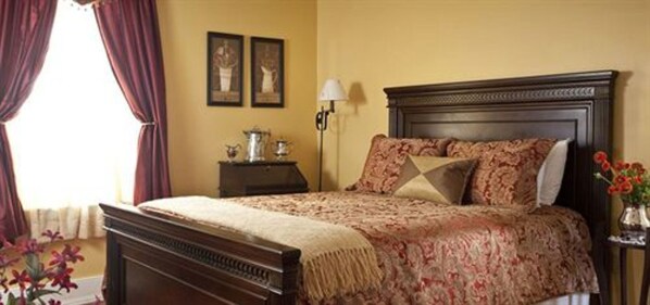 A neatly made bed with a patterned bedspread, a dark wooden headboard, and a nightstand with a lamp and a small table with a vase of flowers.