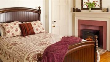 Un dormitorio con cama de madera, ropa de cama floral, chimenea y mesita de noche con lámpara.