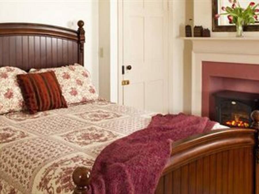 Un dormitorio con cama de madera, ropa de cama floral, chimenea y mesita de noche con lámpara.