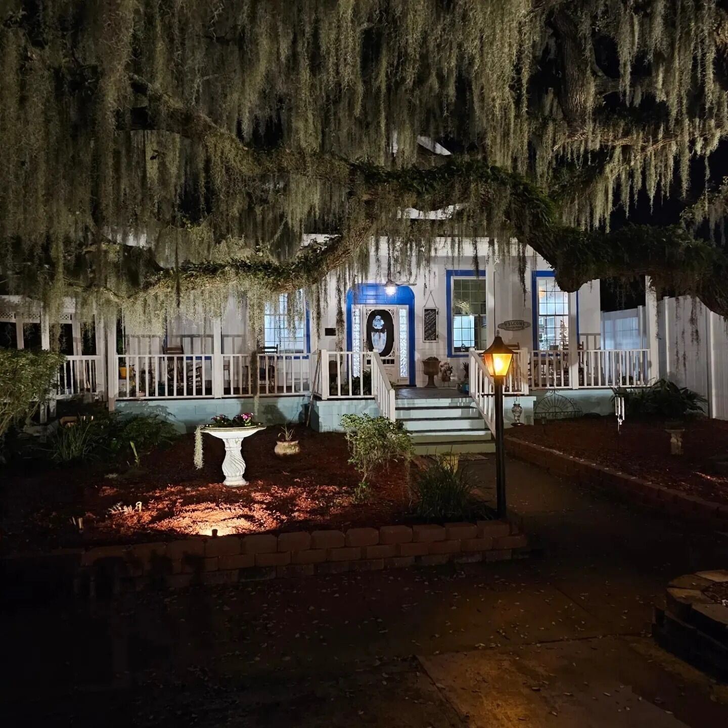 A house with a porch, a welcome sign, and a well-lit entrance.