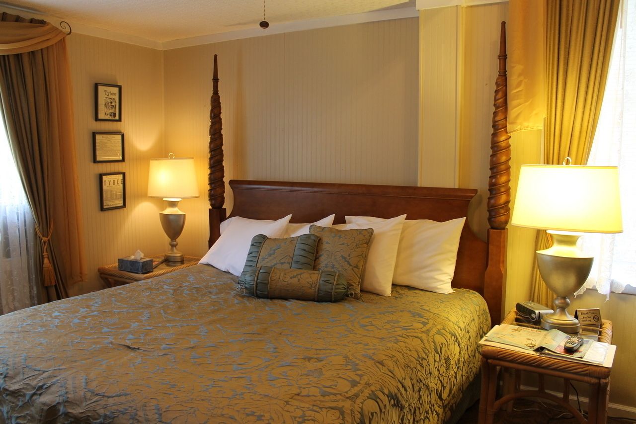 A neatly made bed with a patterned bedspread, two bedside lamps, and a small table with a book and a remote control.