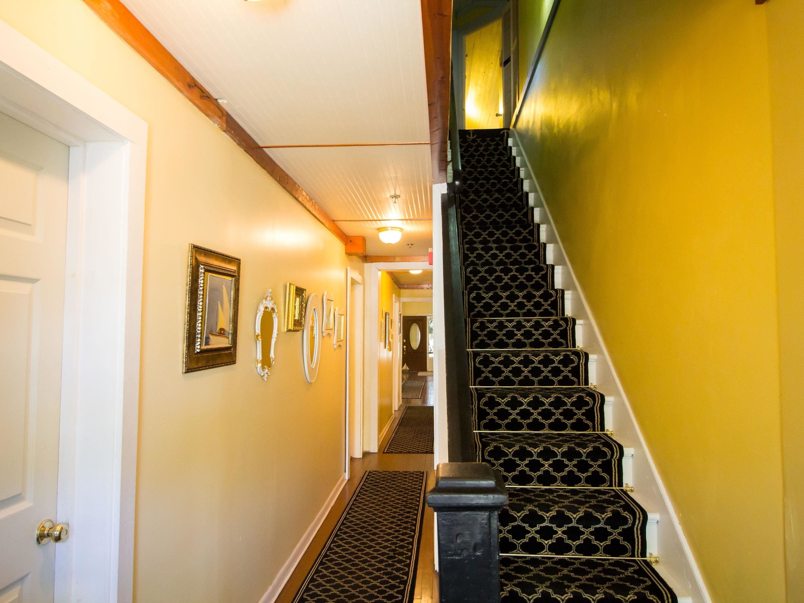 A staircase with black patterned steps and white handrails, leading to a landing with a door and a wall-mounted light fixture.