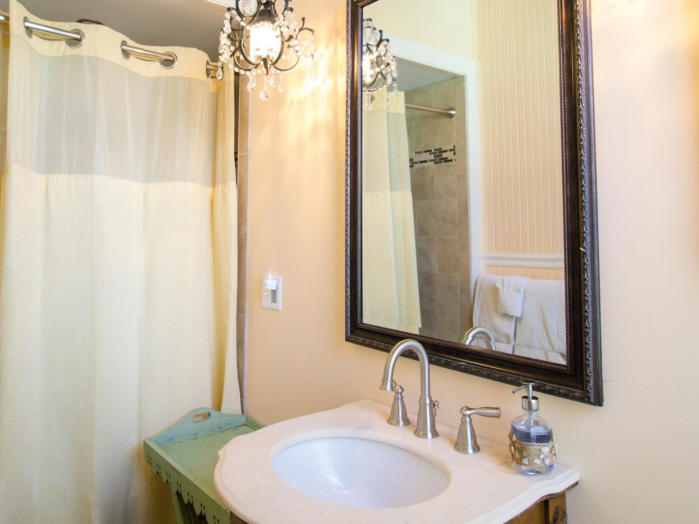 A bathroom with a sink, mirror, chandelier, and shower curtain.