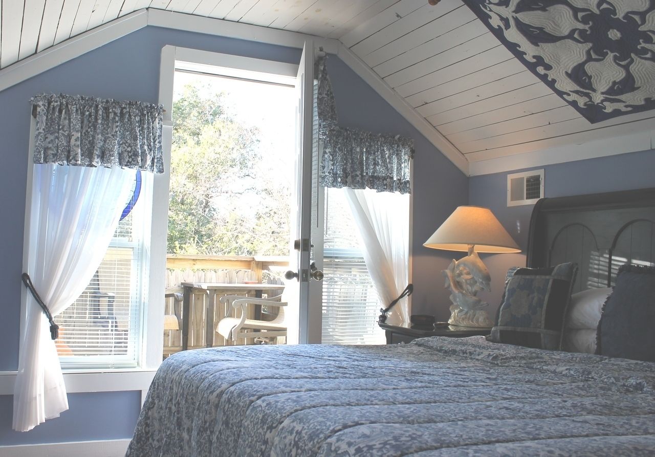 Une chambre à coucher avec un lit, une table de chevet, une lampe et une vue sur l’extérieur.