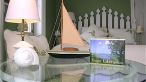 Une chambre à coucher avec un lit, une table de chevet avec une lampe, une petite maquette de bateau et un livre intitulé « Finger Lakes ».