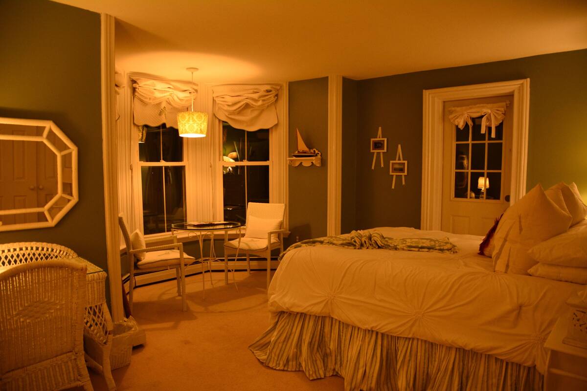 A bedroom with a large bed, two chairs, a small table, and a window with curtains.