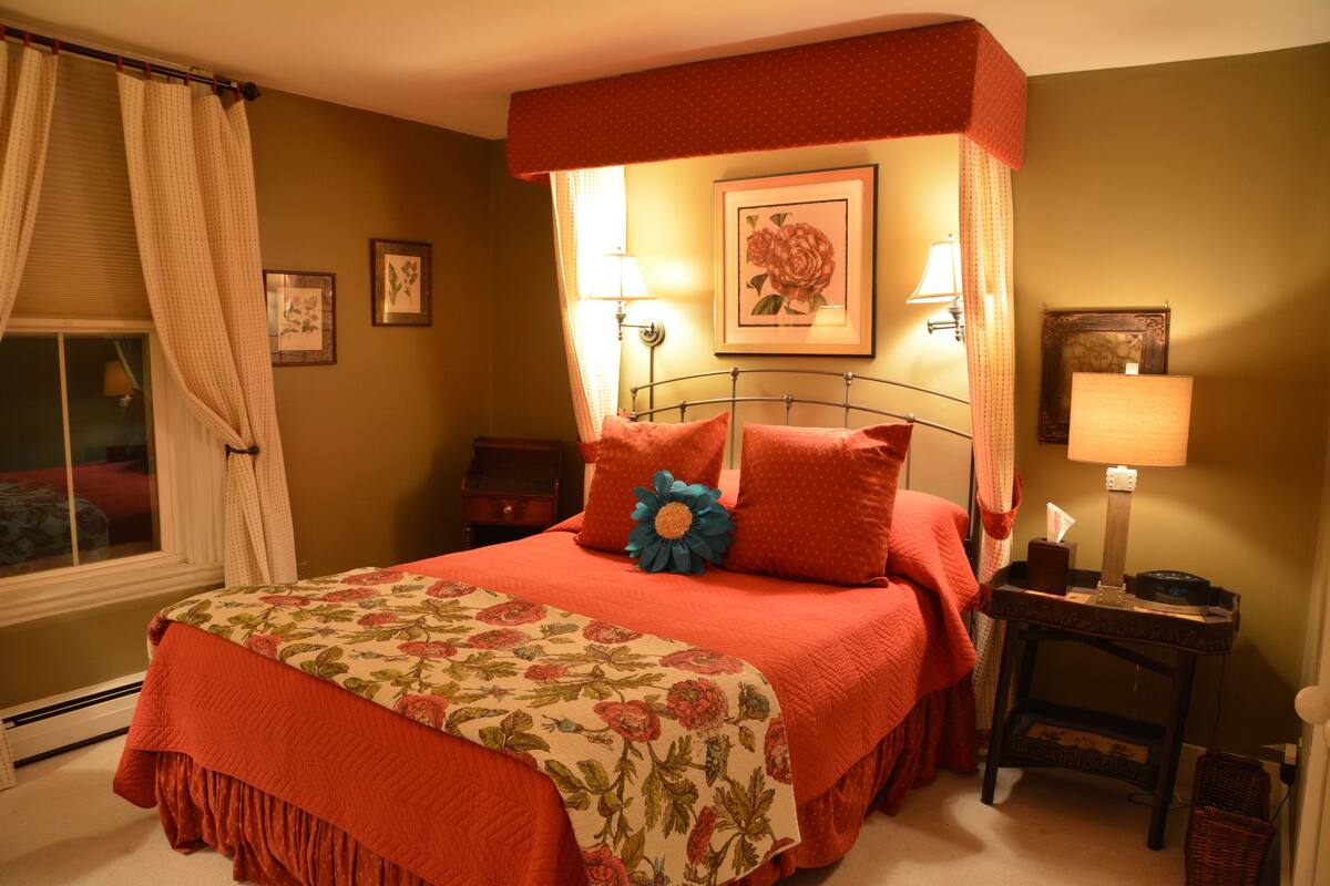 A bedroom with a four-poster bed, floral bedspread, and two bedside lamps.