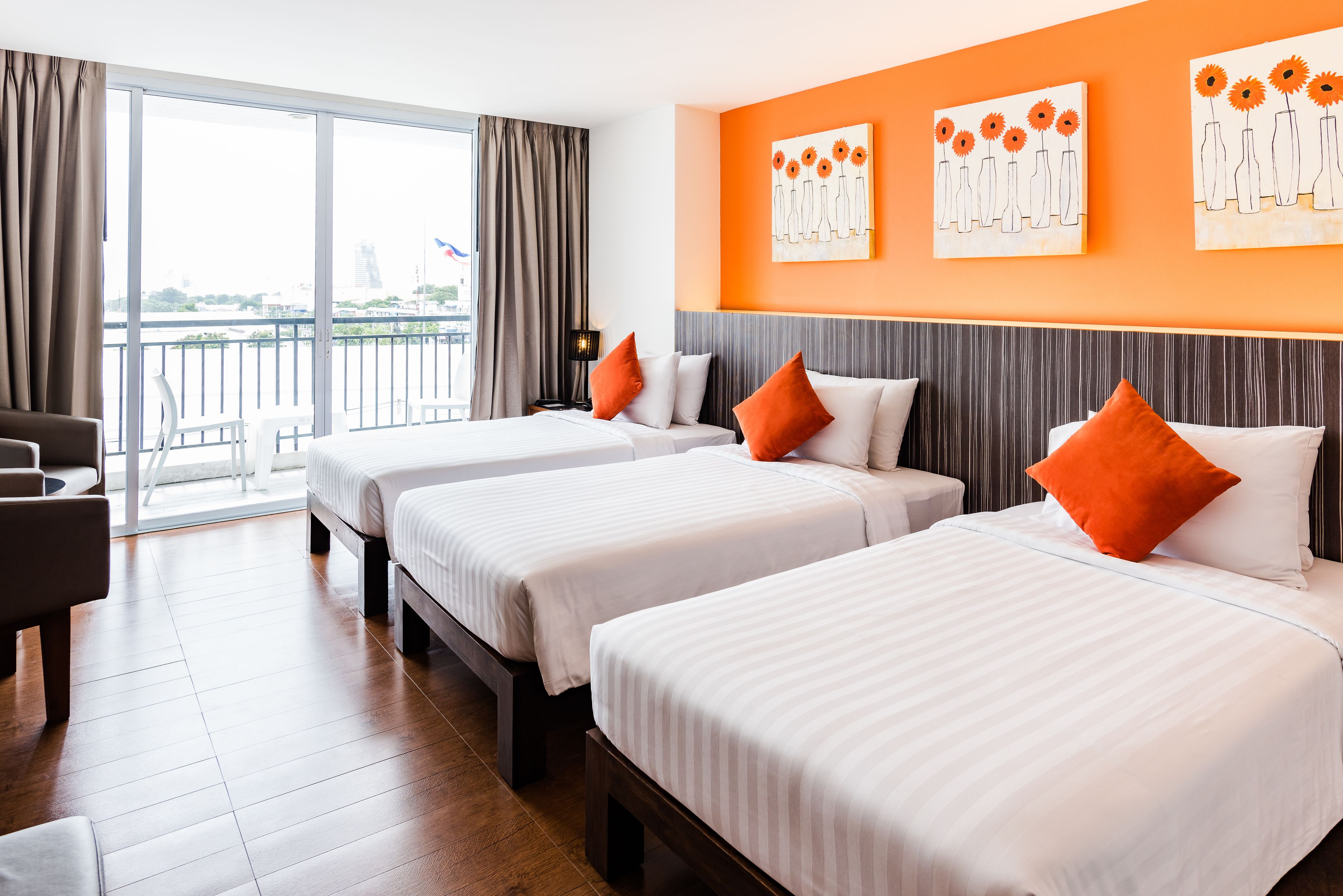 A hotel room with two beds, a sofa, a large window with curtains, and artwork on the wall.