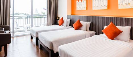 A hotel room with two beds, a sofa, a large window with curtains, and artwork on the wall.