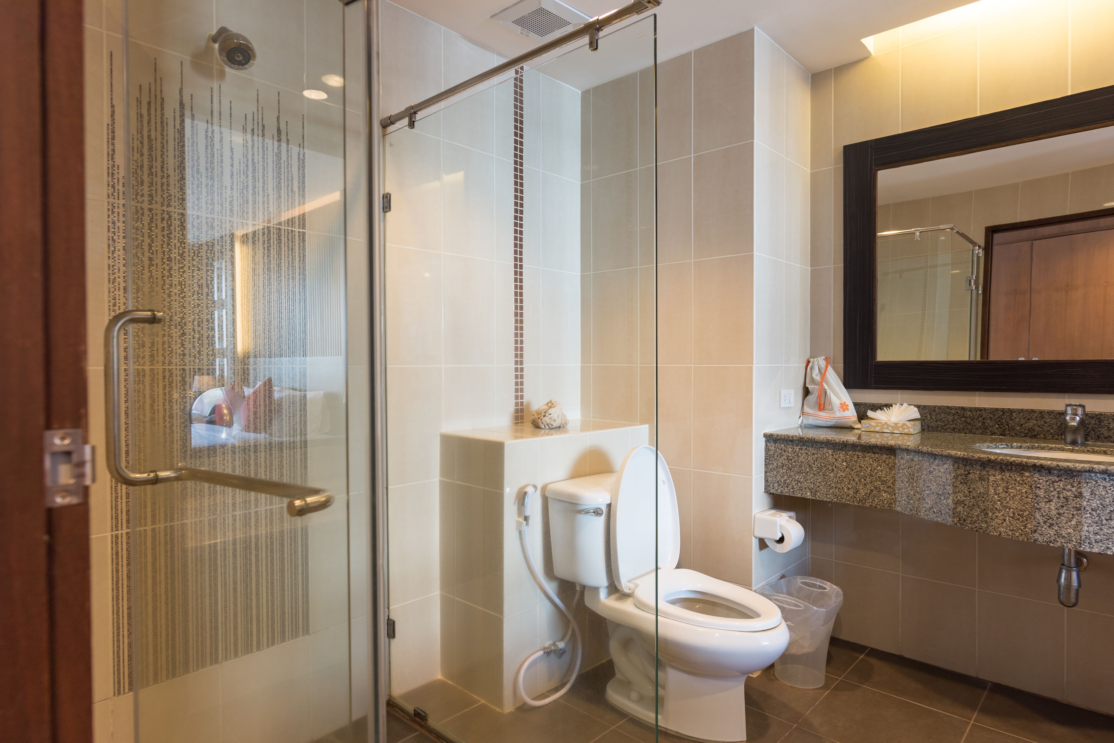 A modern bathroom with a glass shower enclosure, a toilet, and a sink with a granite countertop.