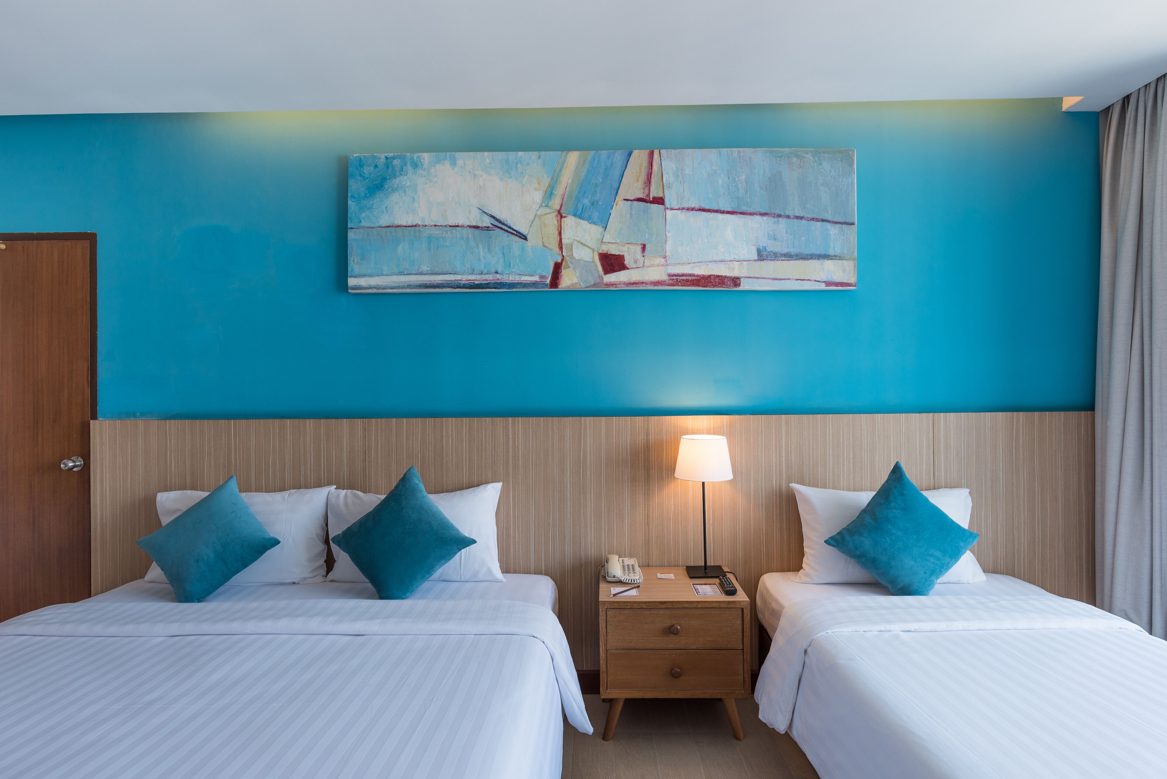 A hotel room with two beds, a nightstand, a lamp, and a painting on the wall.