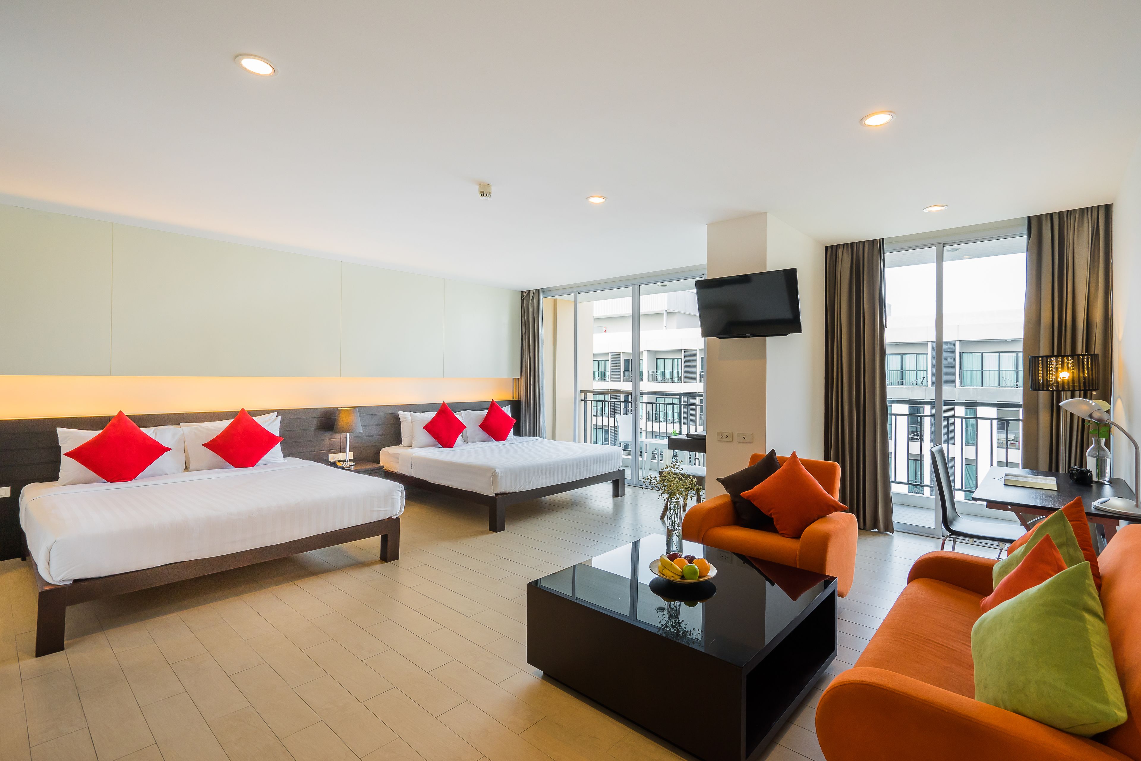Une chambre d’hôtel avec deux lits, un canapé, une table basse avec des fruits et un téléviseur.