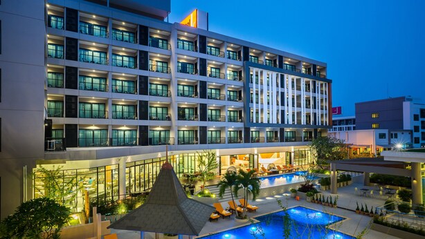 Un hotel con varios pisos, piscinas al aire libre y un patio bien iluminado.