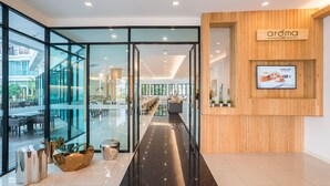 Interior de una cafetería moderna con divisiones de vidrio, una pared de acento de madera y una pantalla digital con el menú.