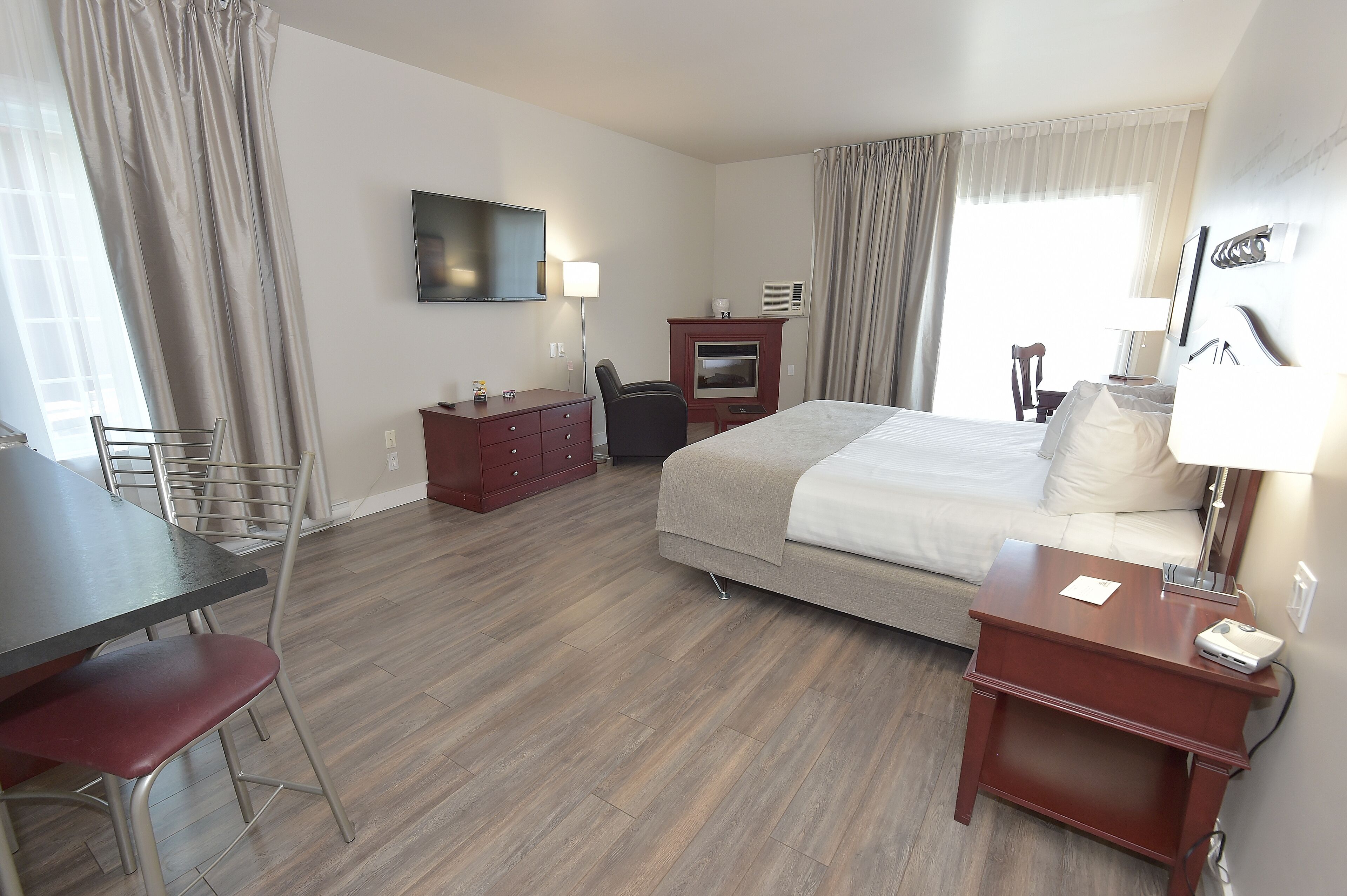 Habitación de hotel con cama, escritorio, silla, televisor y ventana con cortinas.