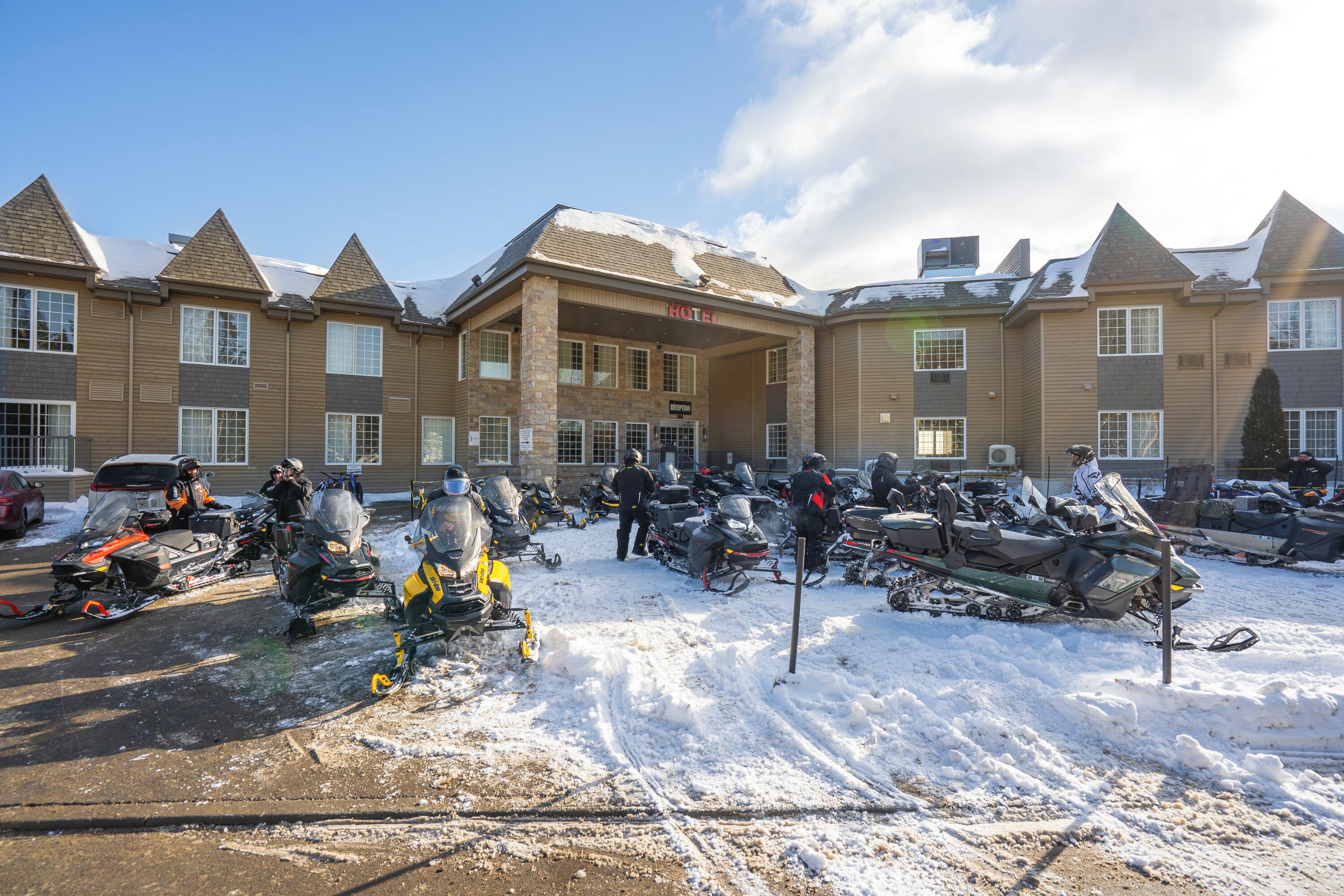 A hotel with multiple buildings, a covered parking area with snow, and several snowmobiles.