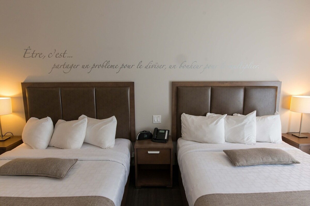 A hotel room with two beds, each with a headboard, bedside lamps, and a wall-mounted phone.