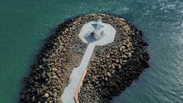 An aerial view of a coastal area with a paved walkway leading to a structure with a geometric roof.