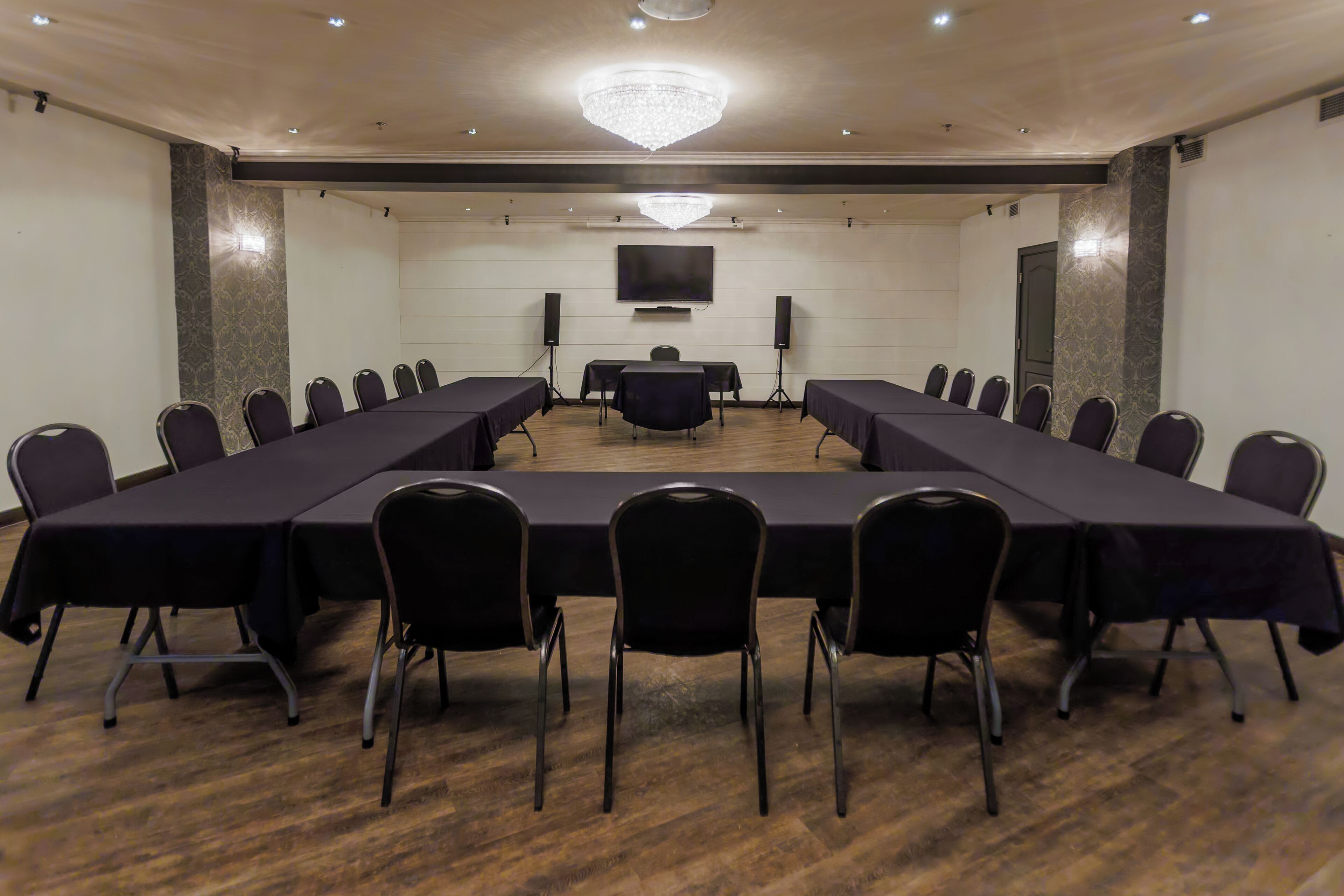 A conference room with a long table, chairs, a chandelier, a TV, and speakers.