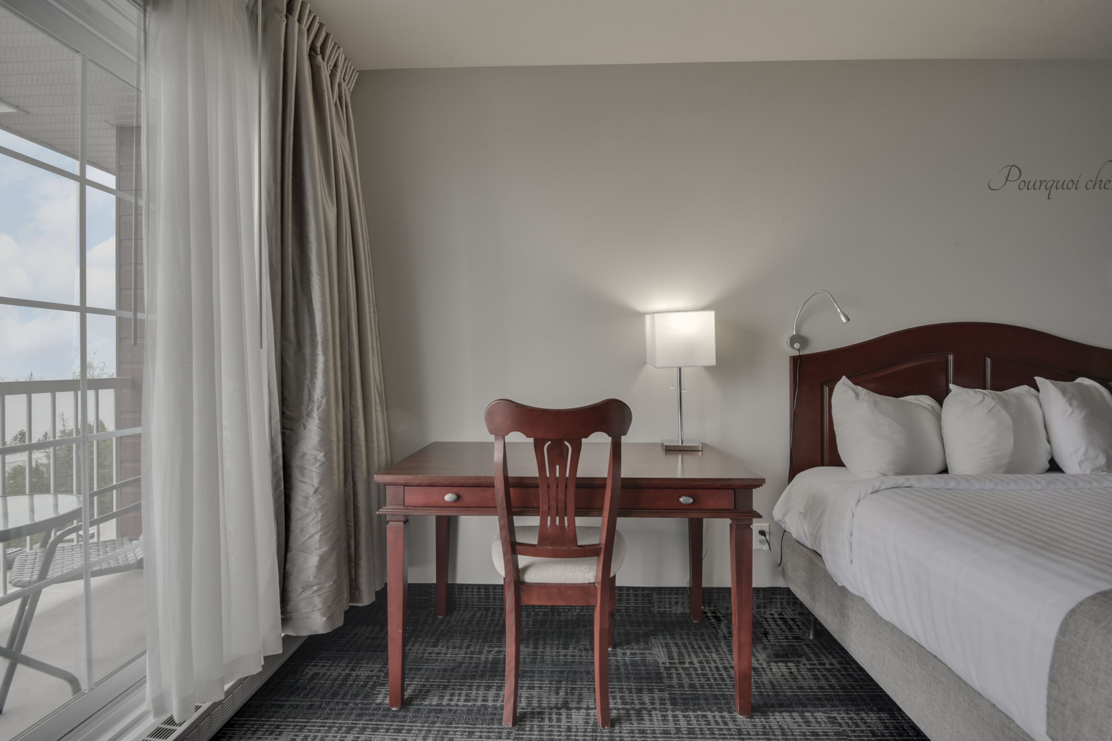 Une chambre d’hôtel avec un lit, un bureau et une chaise, une lampe et une vue sur l’extérieur.