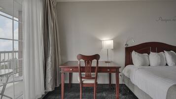 Una habitación de hotel con una cama, un escritorio con una silla, una lámpara y vistas al exterior.