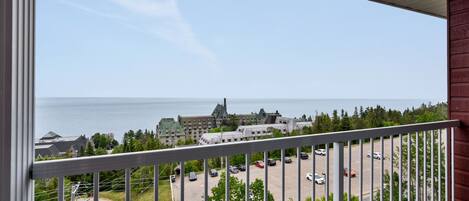 A balcony with a view of a parking lot and a building across the water.
