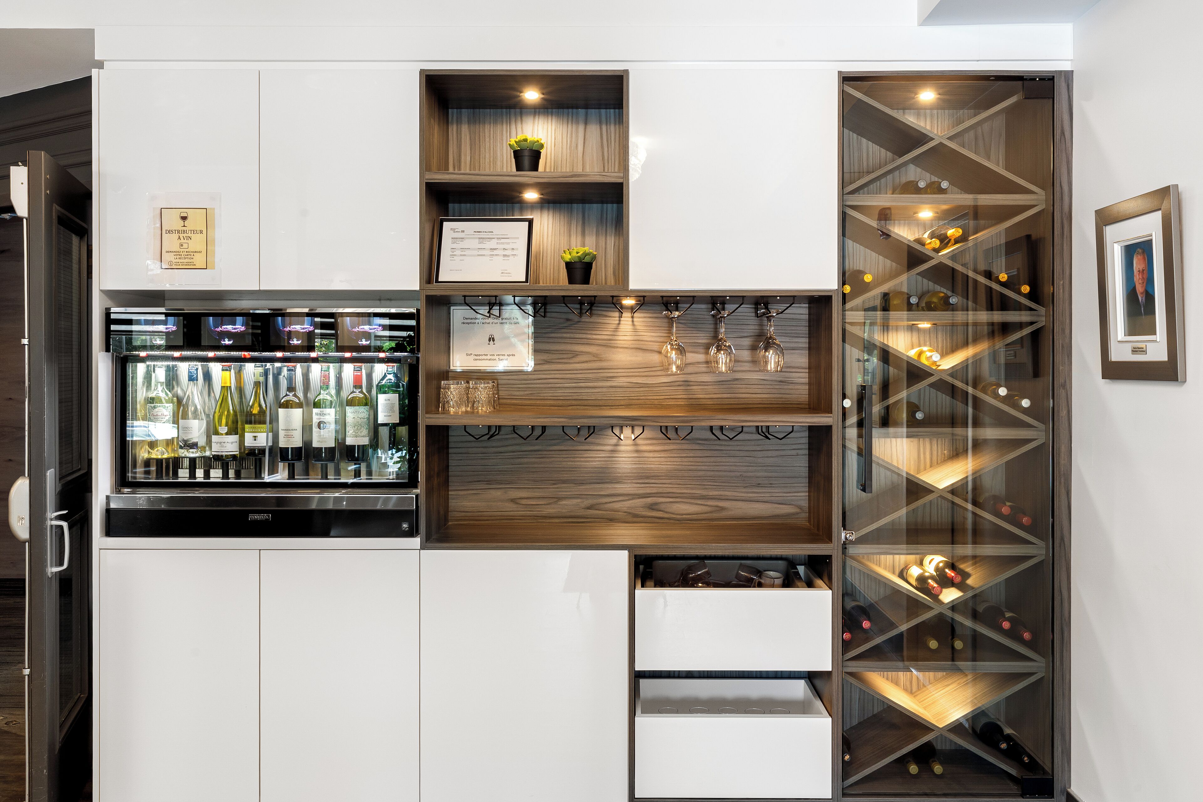 A wine storage unit with multiple shelves and drawers, a refrigerated section with bottles, and a framed picture on the wall.