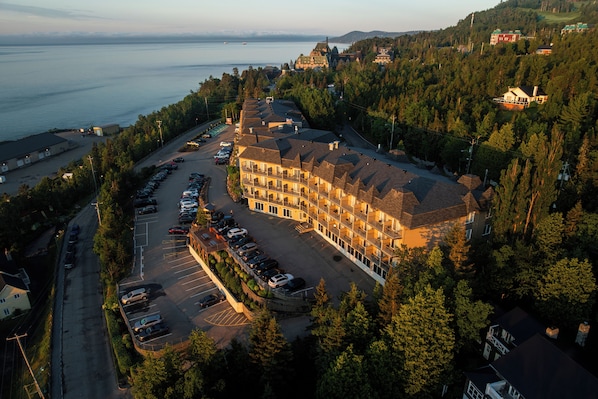 An aerial view of a hotel with multiple buildings, a parking lot, and a body of water in the background.