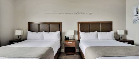 A hotel room with two beds, a bedside table with a lamp, and a wall-mounted artwork.