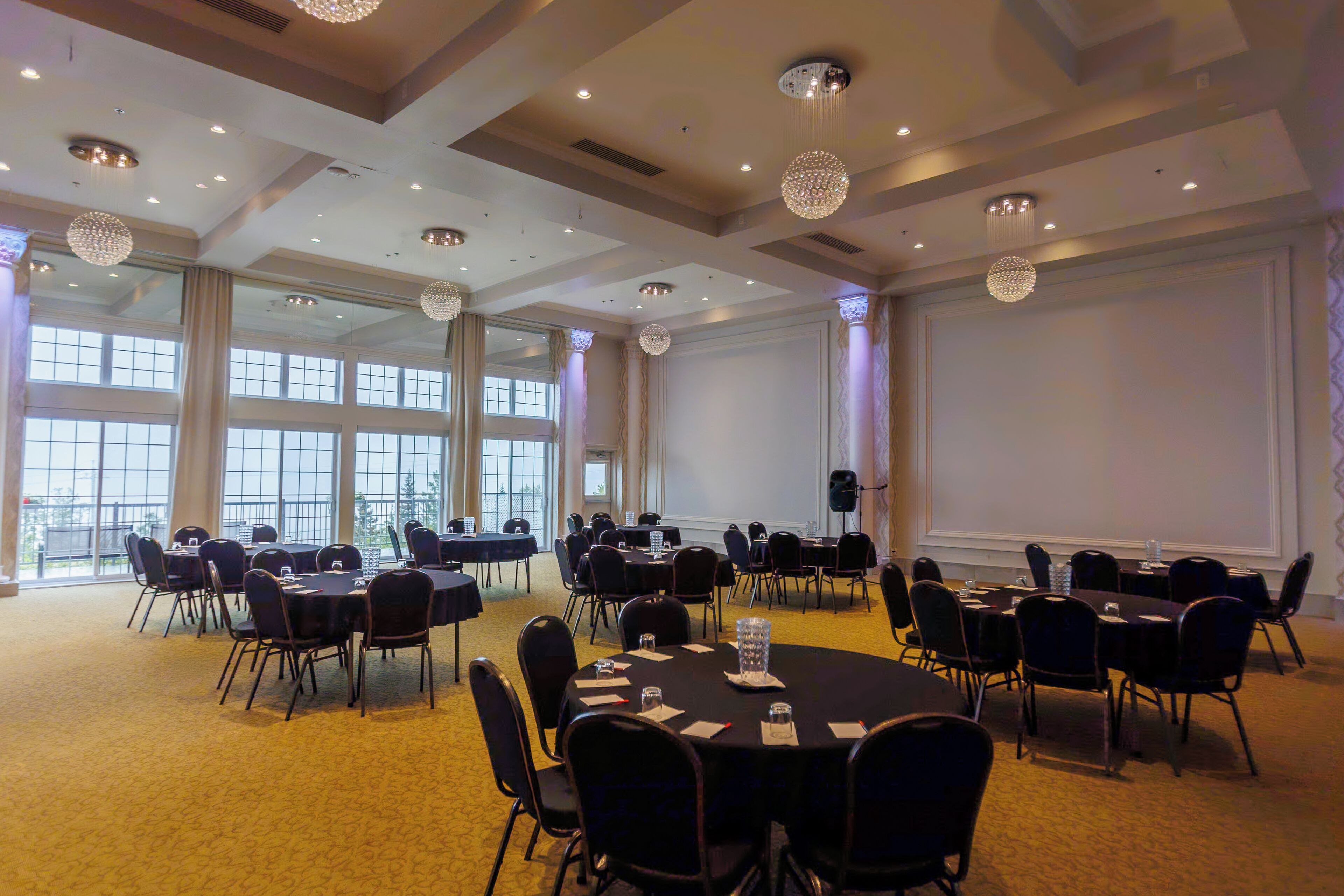 Un salón de conferencias con varias mesas y sillas, ventanas amplias y candelabros.