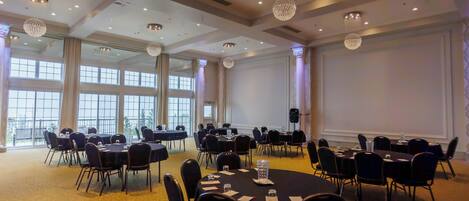 Un salón de conferencias con varias mesas y sillas, ventanas amplias y candelabros.