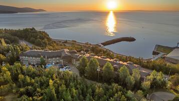 A coastal hotel with multiple buildings, a parking area, and a view of the sea during sunset.
