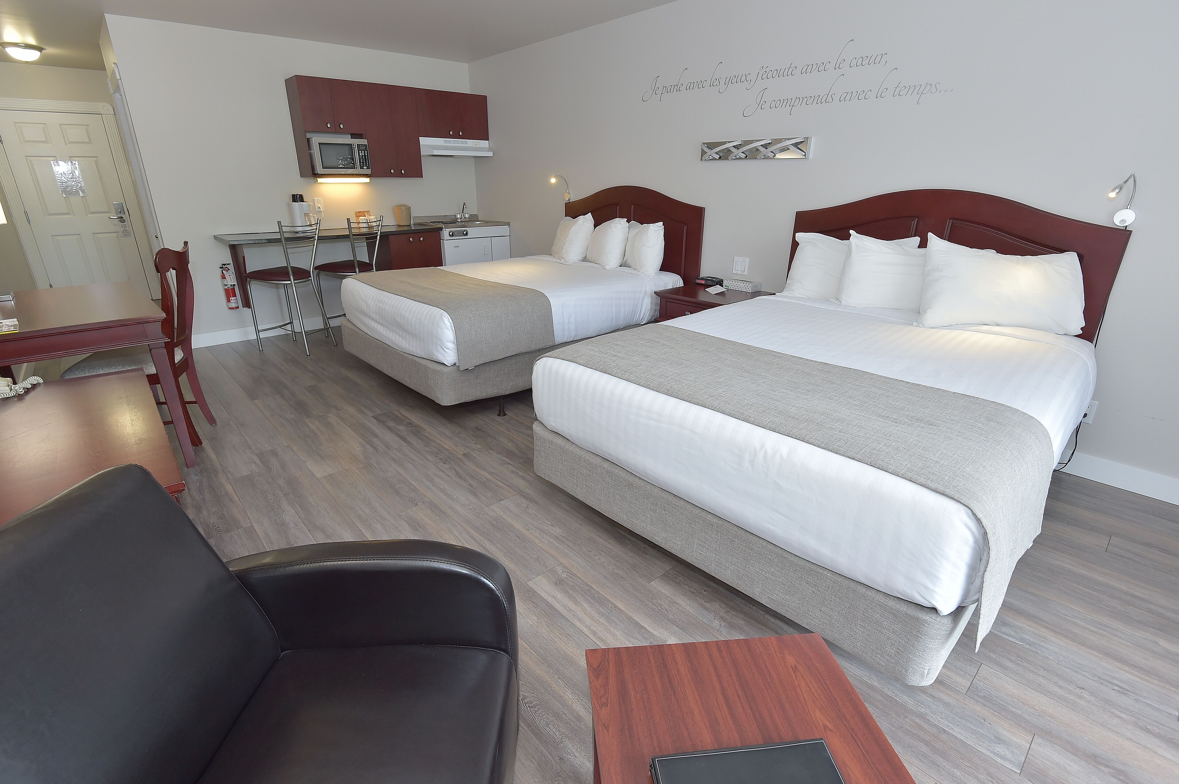 A hotel room with two beds, a desk, a chair, and a kitchenette.