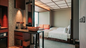 Una habitación de hotel moderna con una zona de cocina, una cama con ropa blanca y un ventanal grande.