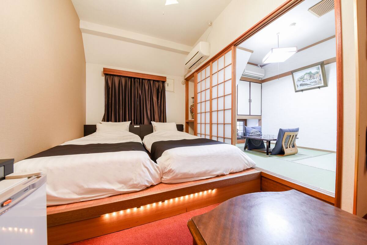 Une chambre d’hôtel avec un lit, un banc en bois, une table et une porte coulissante donnant sur un balcon.