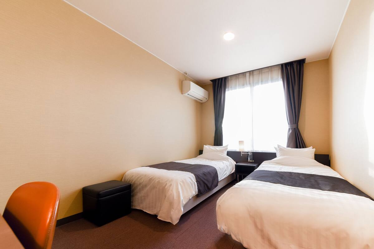 Une chambre d’hôtel avec deux lits, un bureau, une chaise et une fenêtre avec des rideaux.