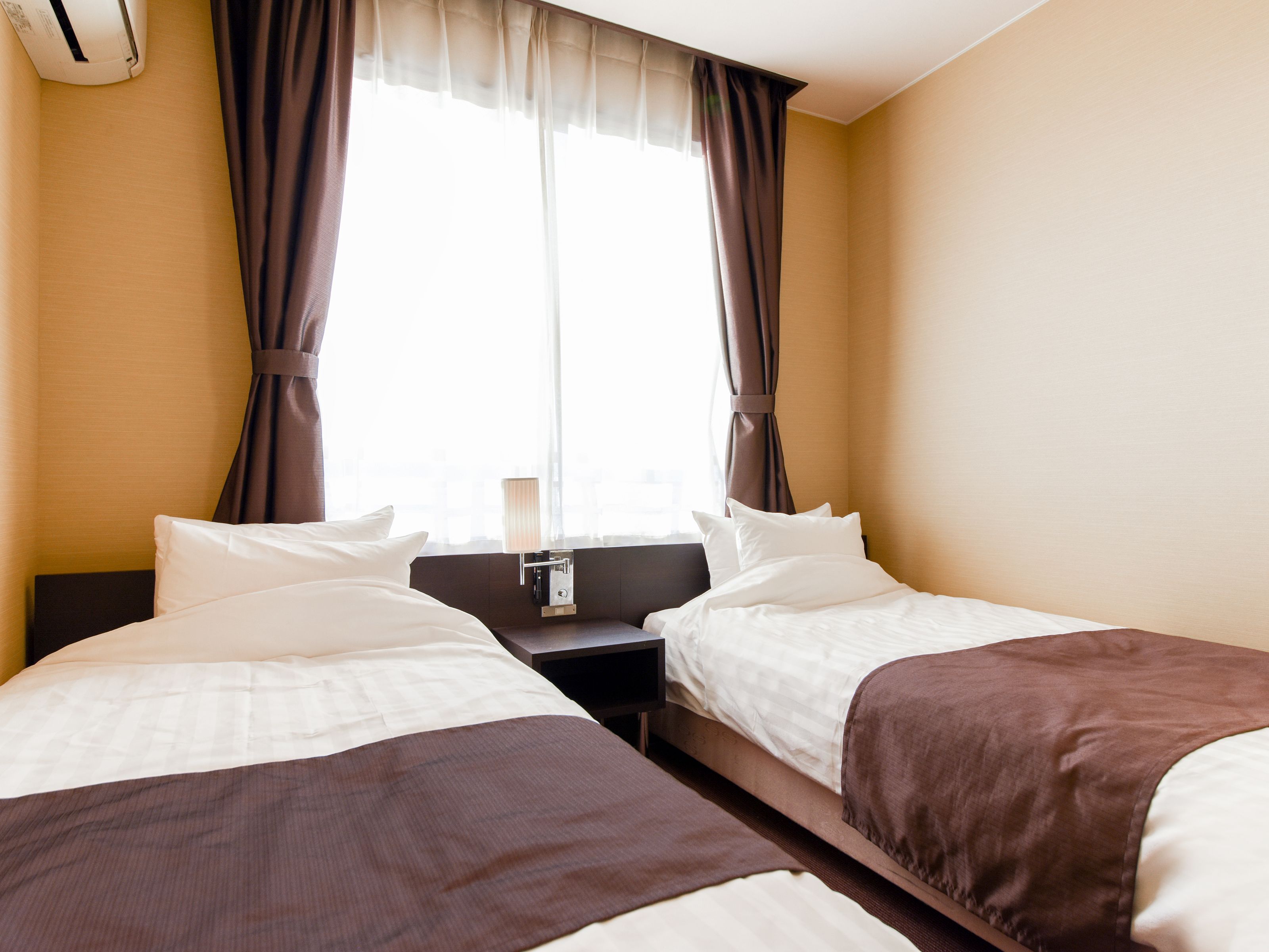 A hotel room with two beds, a nightstand, and a window with curtains.