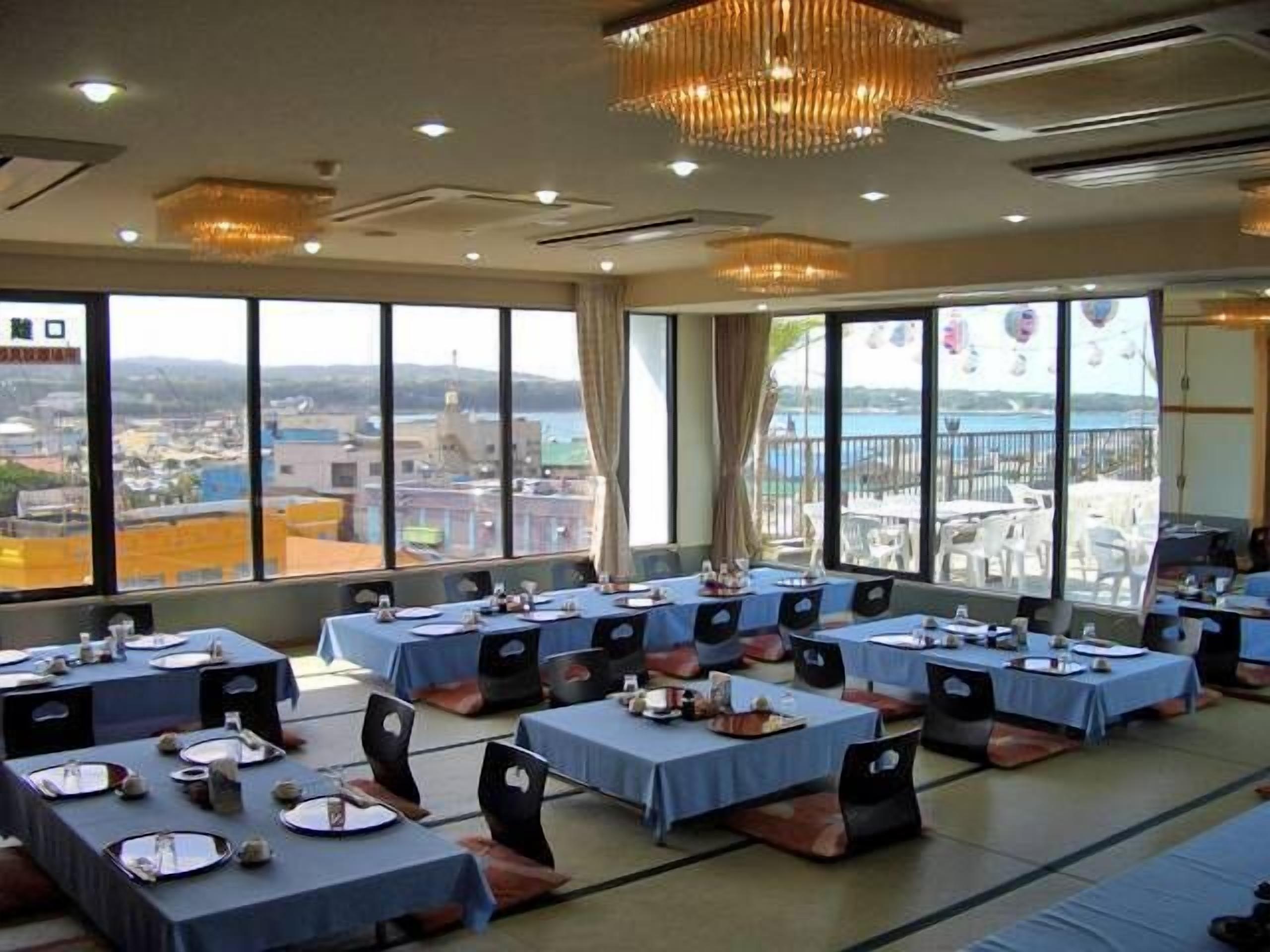 Une salle de conférence équipée de plusieurs tables disposées pour une réunion, de grandes fenêtres offrant une vue sur le paysage urbain et un lustre suspendu au plafond.