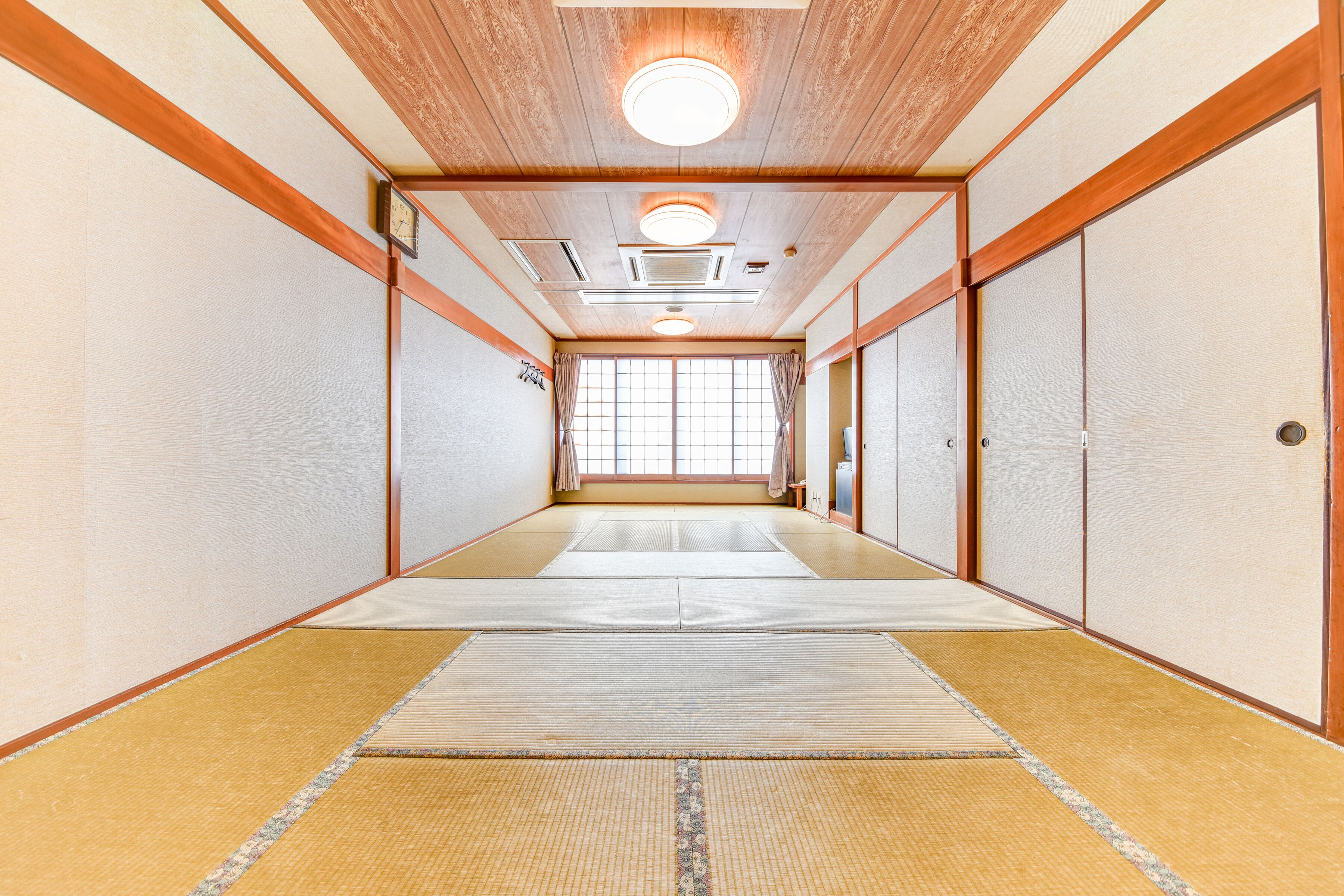 Une pièce de style japonais traditionnel, avec un sol recouvert de tatamis, des portes coulissantes et un plafond en bois doté d’un éclairage encastré.