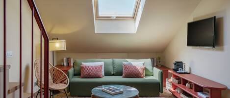 A cozy living room with a green sofa, a round coffee table, a bookshelf, and a TV mounted on the wall.