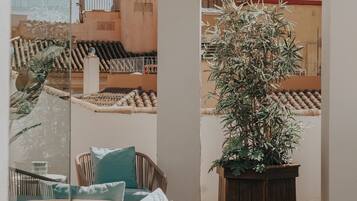 Un área de estar al aire libre con mobiliario de mimbre y una planta en maceta, con vistas a un edificio histórico con un campanario.