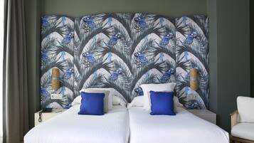 Una habitación de hotel con dos camas, un cabecero de estilo tropical, una mesita de noche con lámpara y una silla.