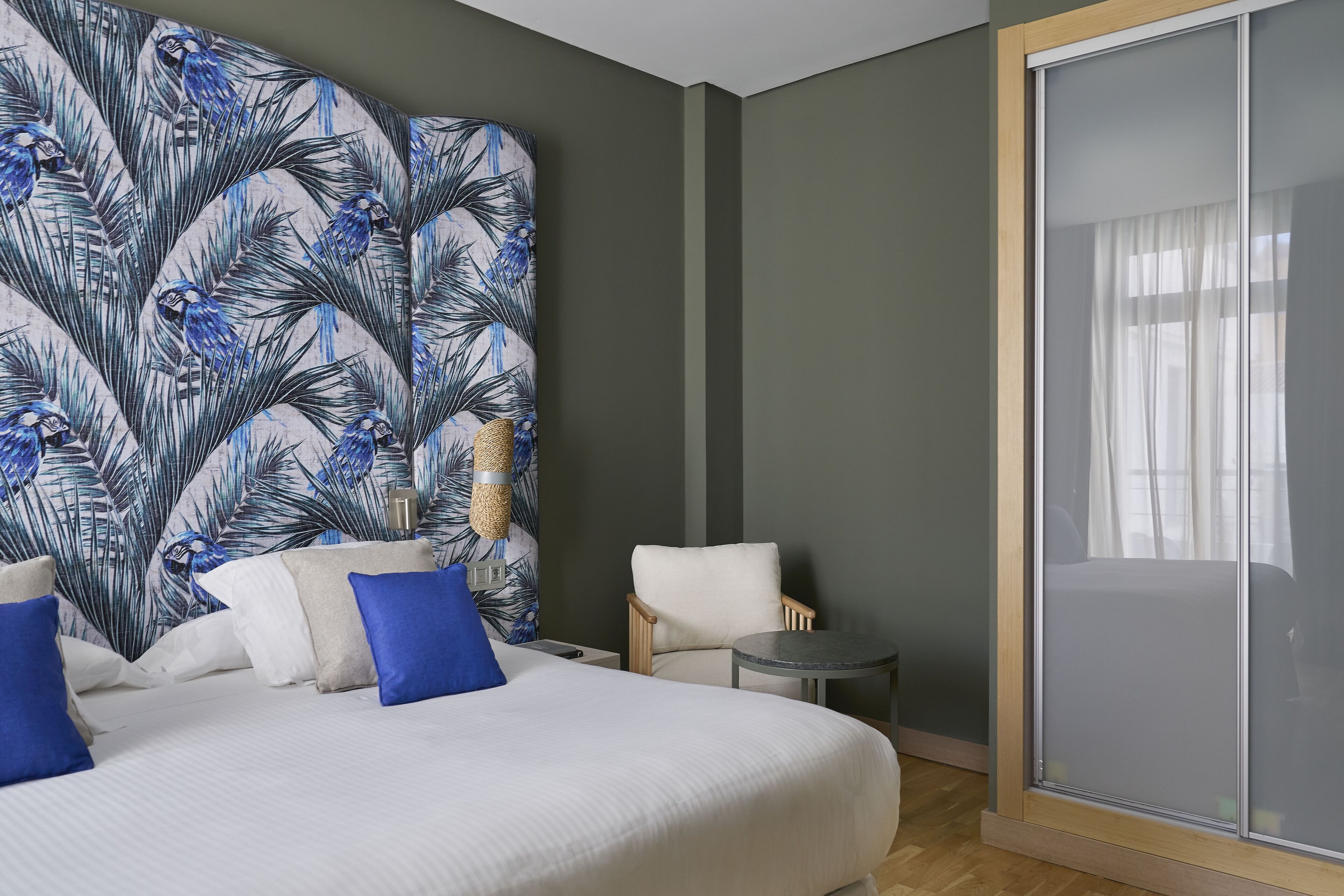 A hotel room with a large bed, a chair, a small table, and a large window with a view.