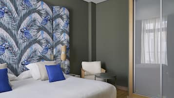 A hotel room with a large bed, a chair, a small table, and a large window with a view.