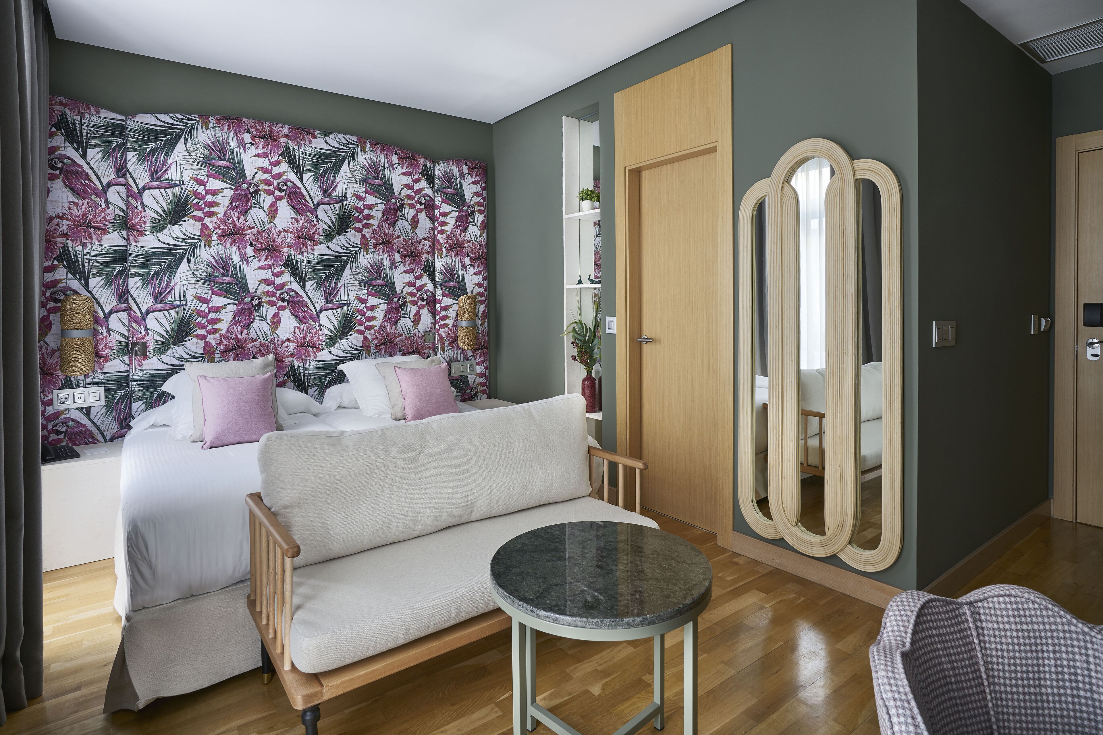 A bedroom with a bed, a sofa, a round table, a mirror, and a wardrobe.