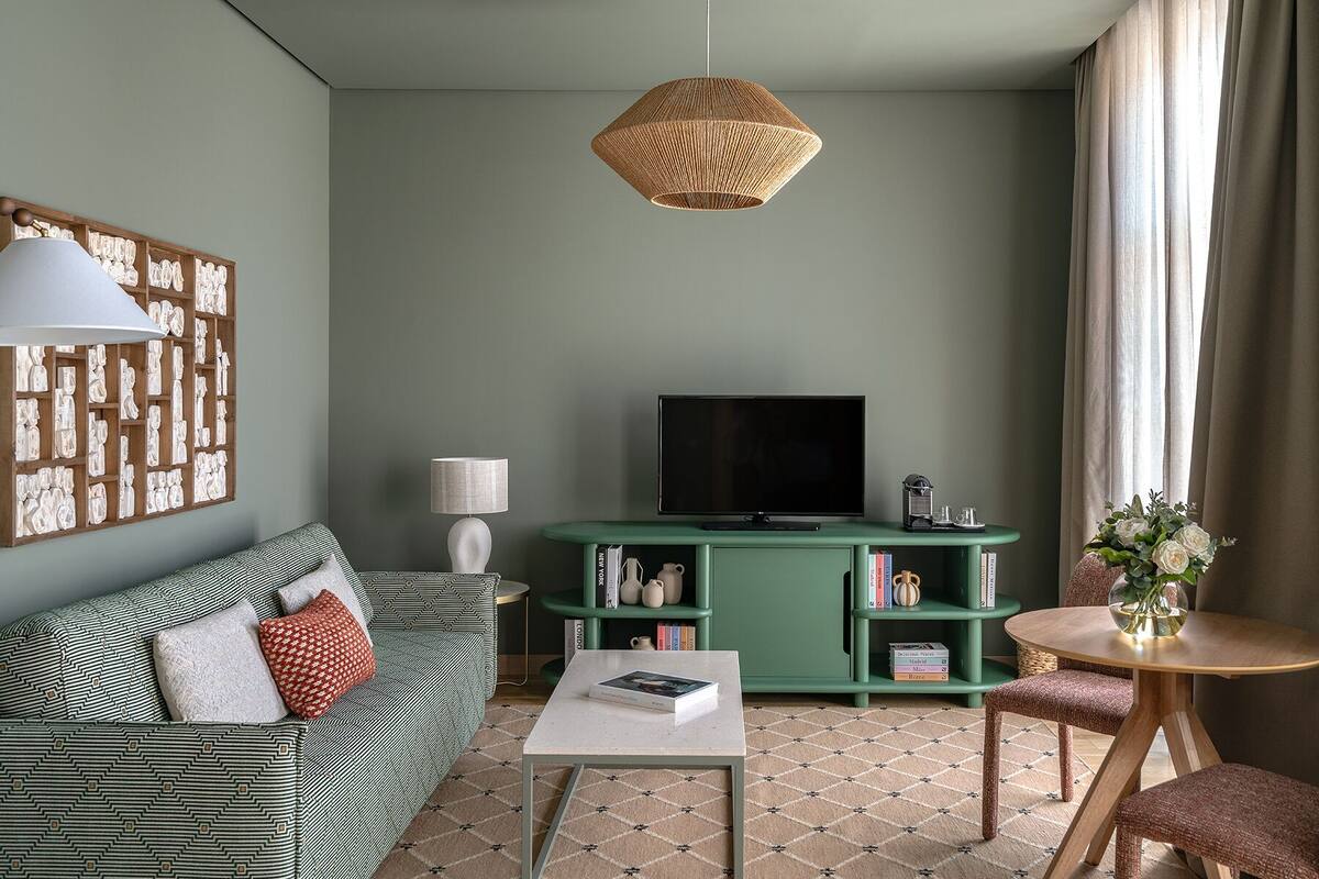A living room with a green sofa, a coffee table, a TV on a green stand, a wicker pendant light, and a bookshelf.