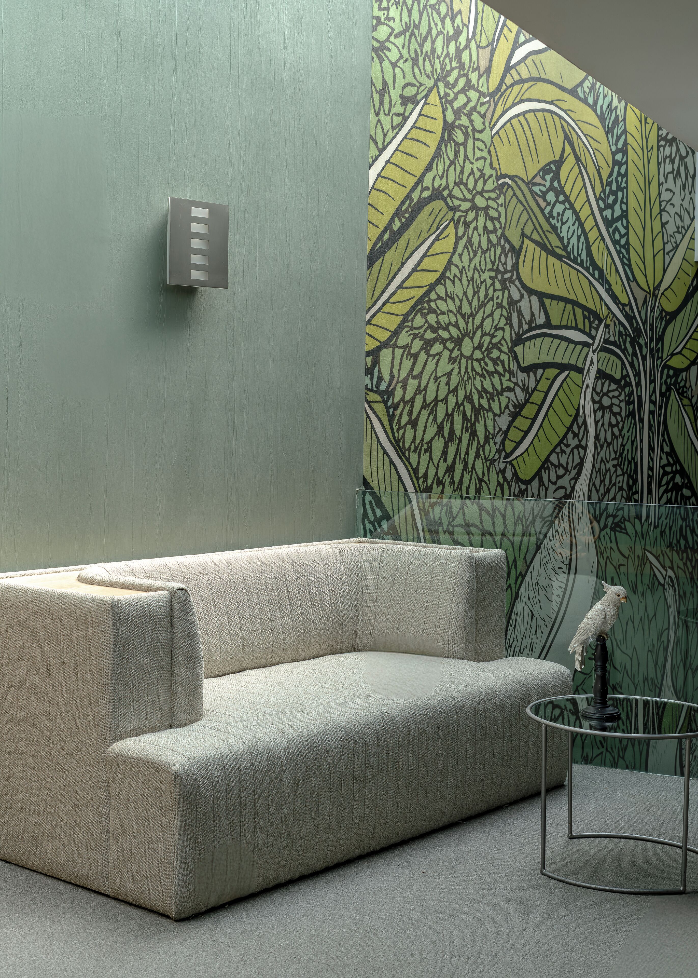 Una sala moderna con un sofá gris, una mesa de centro de vidrio transparente y un interruptor de luz montado en la pared.